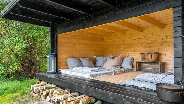 Ein gemütliches Blockhaus mit einem Bett, Kissen, einer Laterne und einem Topf auf dem Boden.