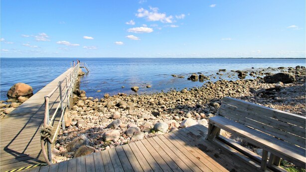Un muelle de madera que se adentra en aguas tranquilas, rodeado de rocas y un banco.