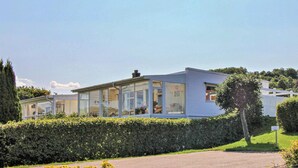 Una casa moderna con grandes ventanales de vidrio, fachada blanca y un jardín cuidado.