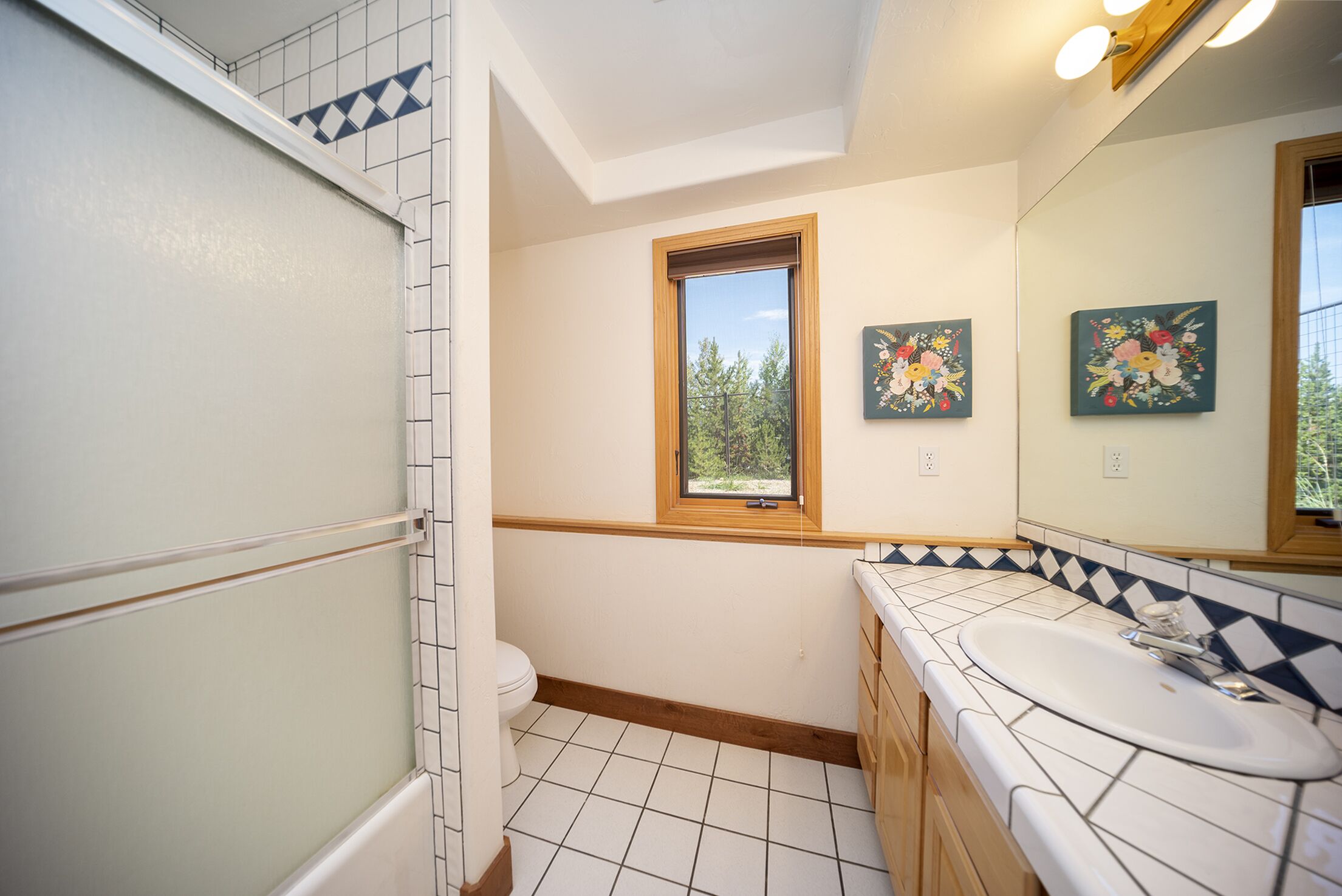 Une salle de bain avec un lavabo blanc, un meuble-lavabo en bois et une fenêtre donnant sur les arbres.