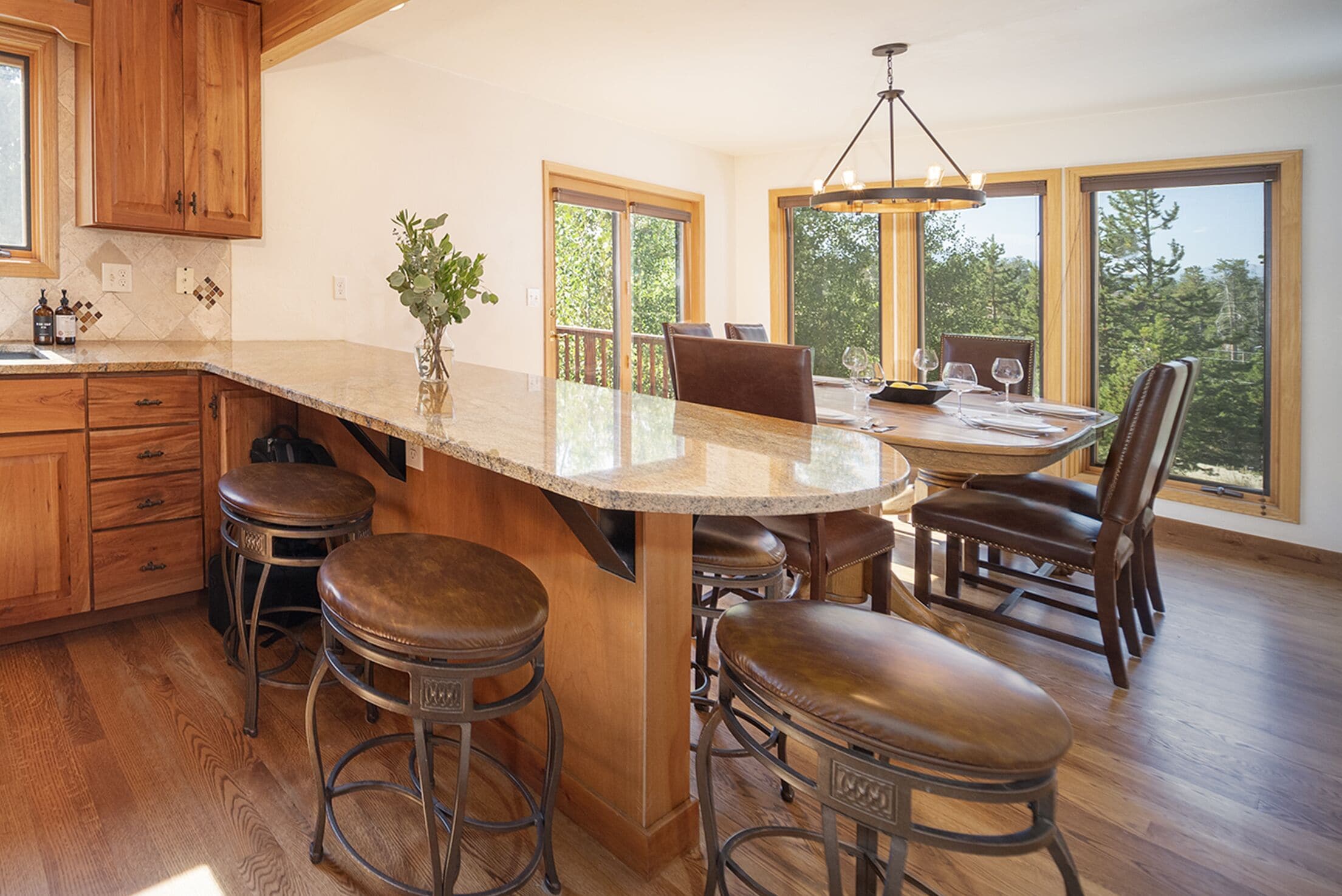 A kitchen with a large island, bar stools, wooden cabinets, and large windows offering a view of the outdoors.
