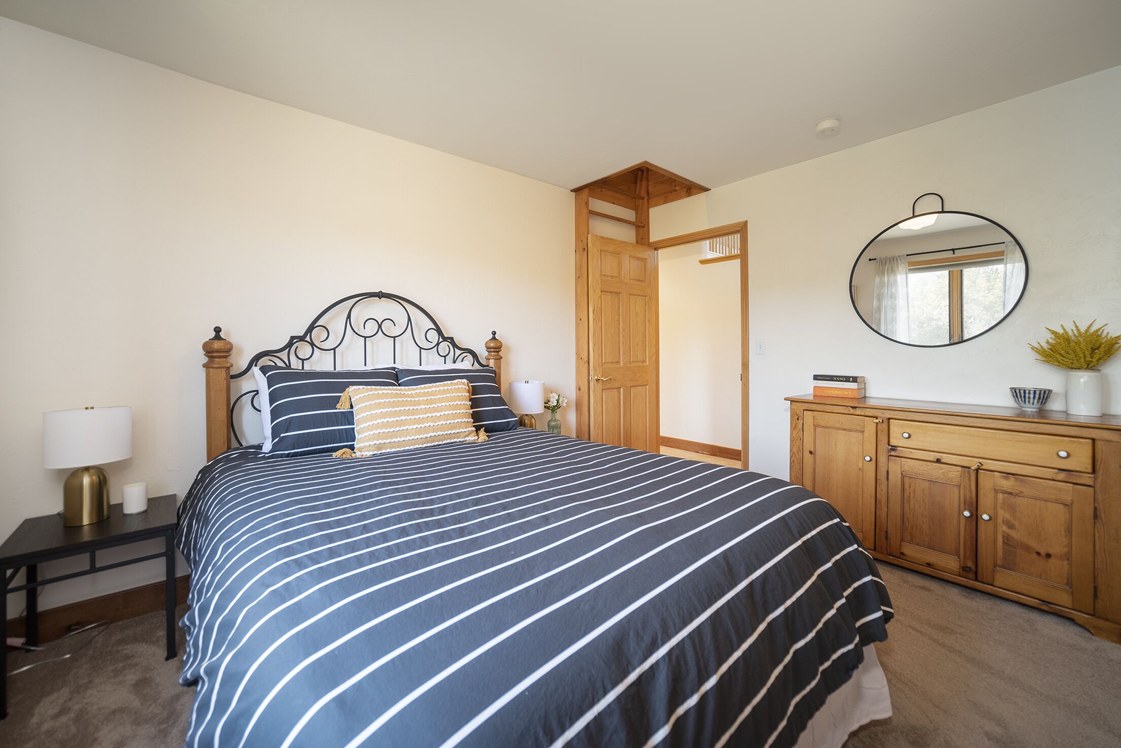 A bedroom with a bed, a nightstand, a dresser, a mirror, and a door.