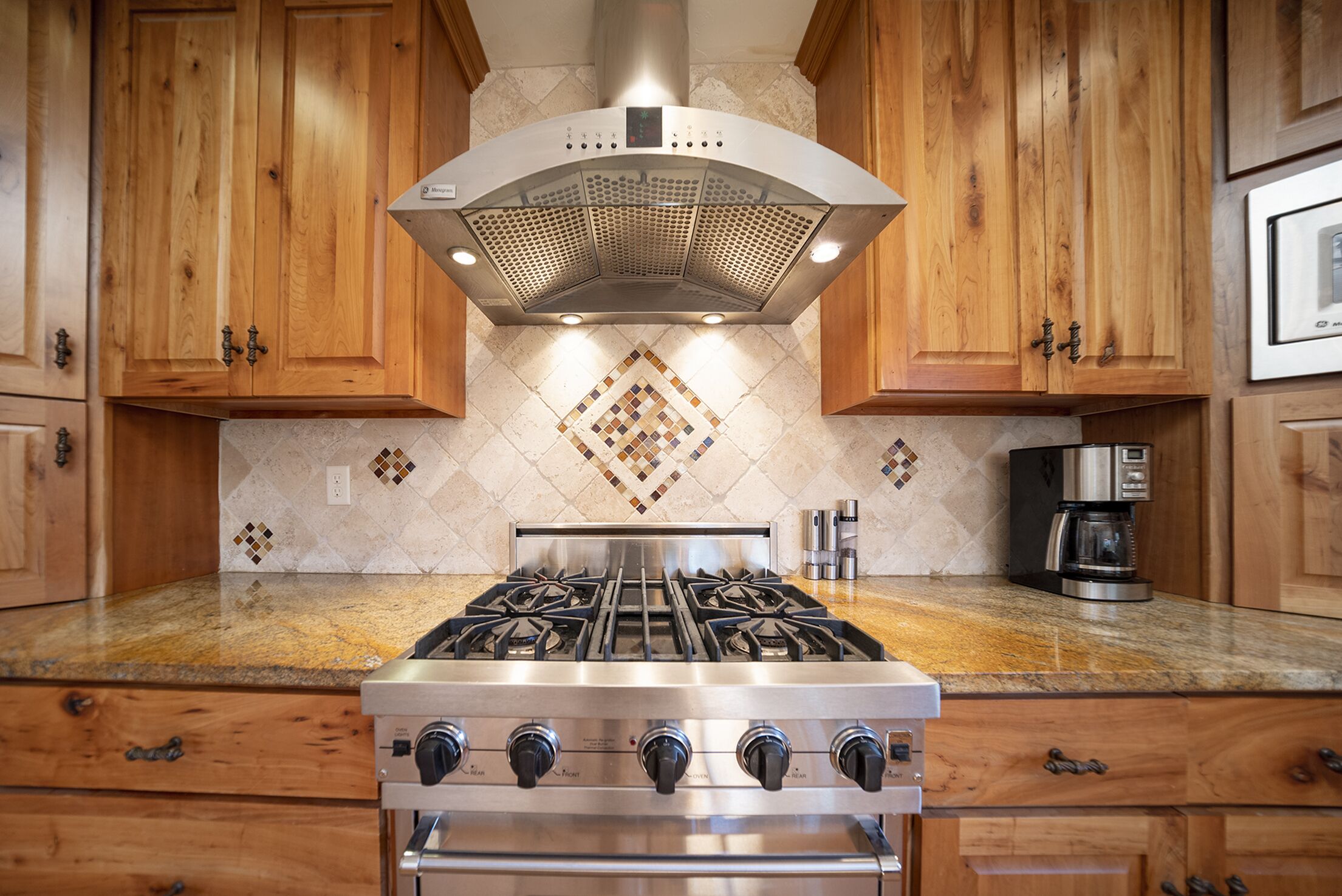 A kitchen with wooden cabinets, a gas stove, a range hood, and a tiled backsplash.
