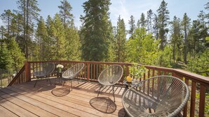 Une terrasse en bois, avec des chaises en métal et une petite table, entourée d’une forêt.