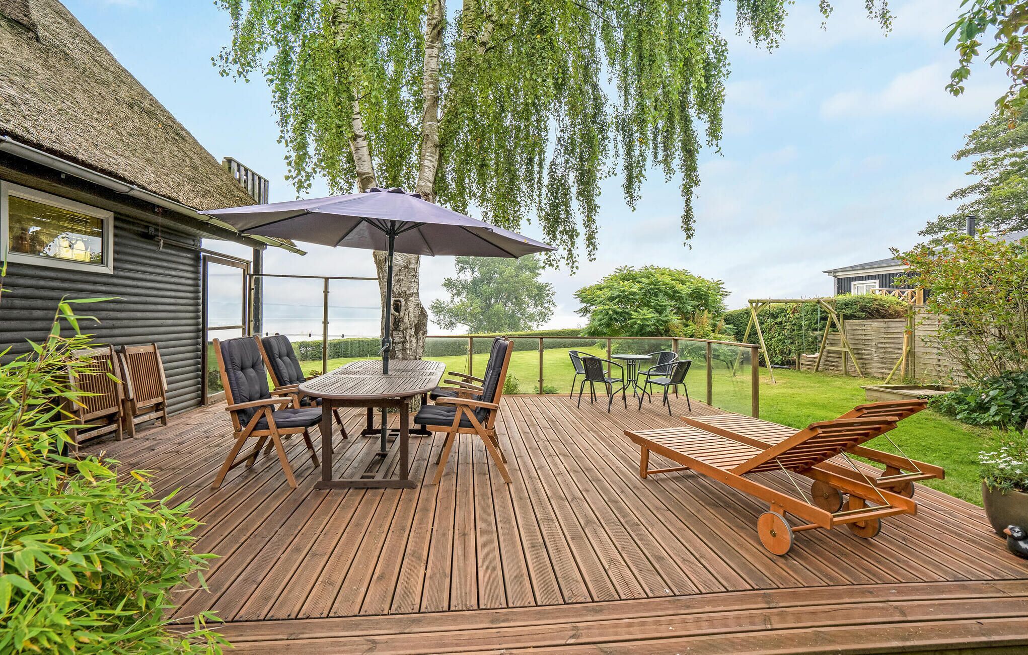 Eine Holzterrasse mit Tisch und Stühlen, einem Sonnenschirm und Blick auf den Garten.