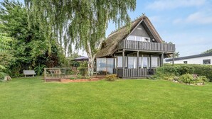 Ein reetgedecktes Haus mit Balkon, umgeben von einem gepflegten Garten und einem See.