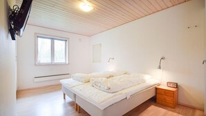 A bedroom with a bed, a bedside table, a lamp, a window, and a wall-mounted TV.