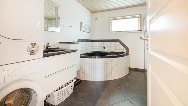 A compact bathroom with a washing machine, a sink, a bathtub, and a window.