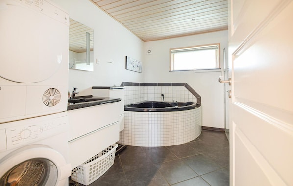 A compact bathroom with a washing machine, a sink, a bathtub, and a window.