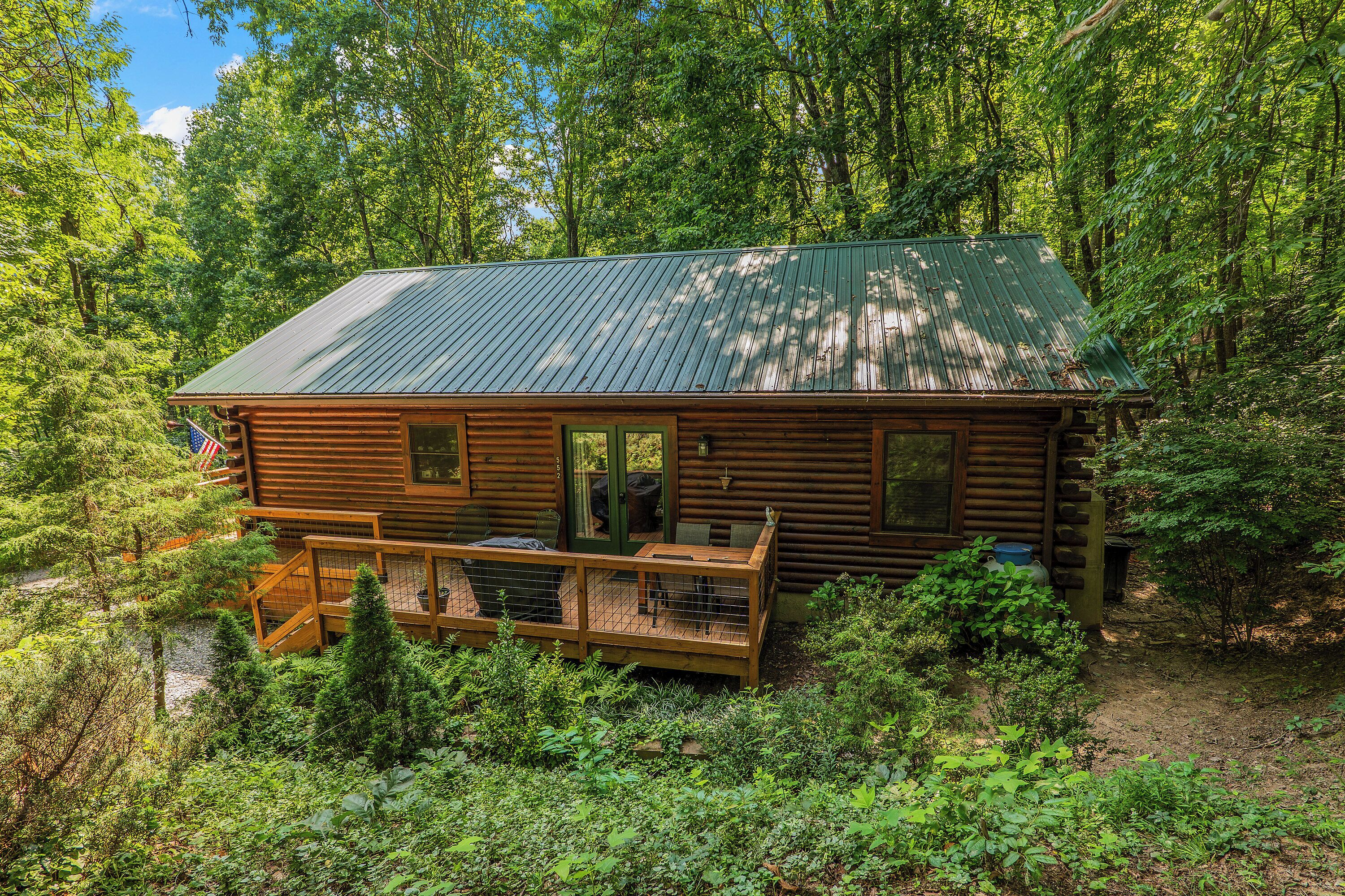 A log cabin with a porch, surrounded by dense forest.
