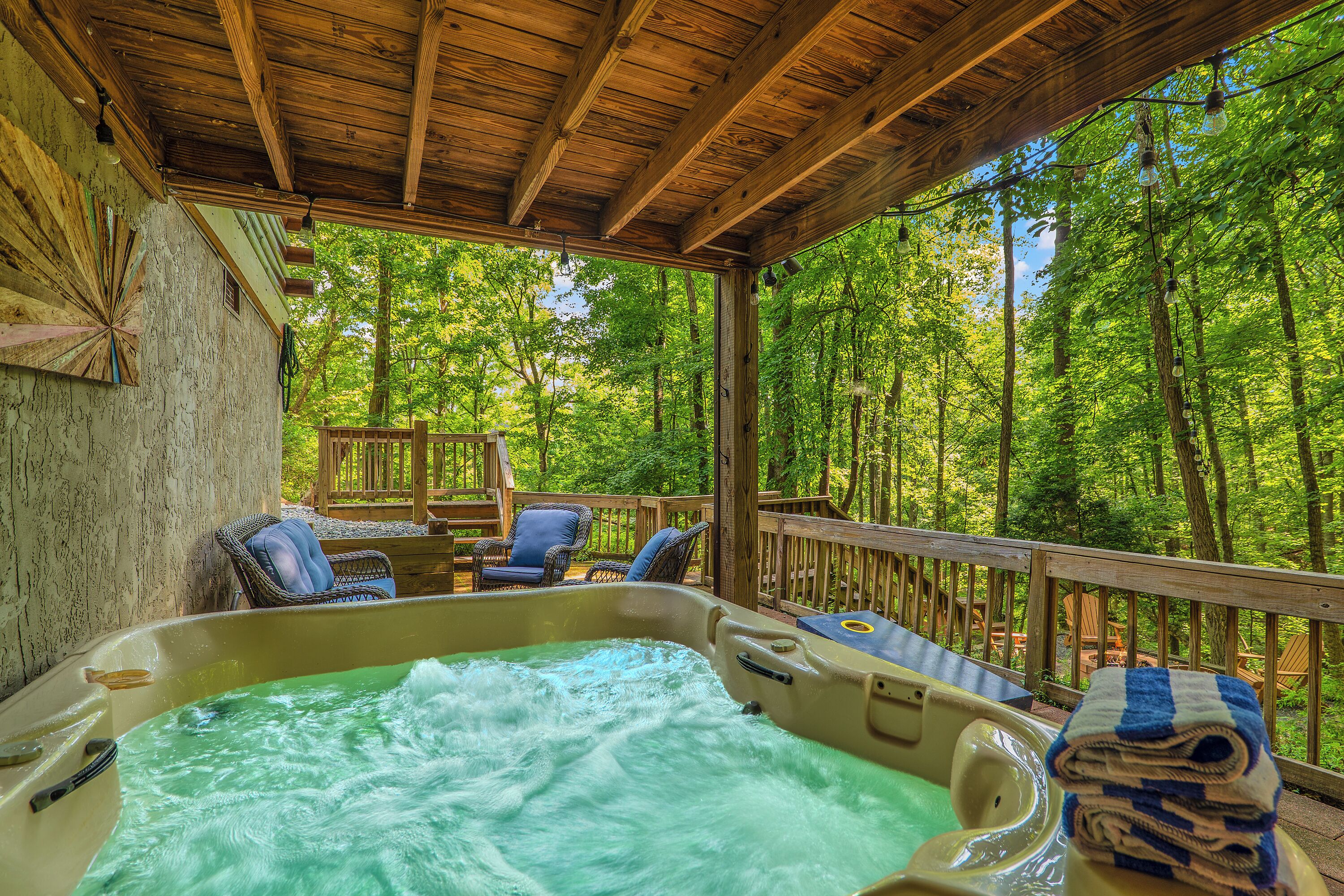 A hot tub area with wooden deck and chairs, surrounded by a forest.