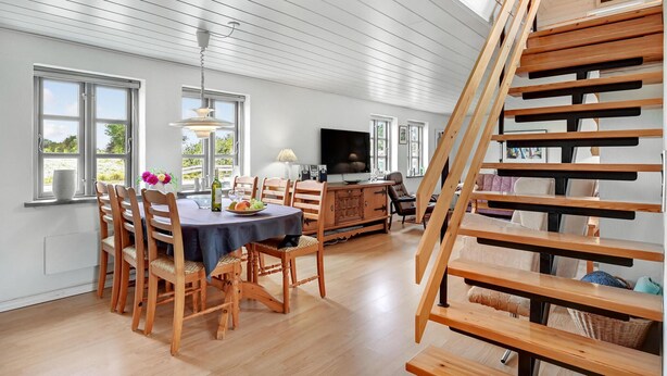 A spacious living area with a dining table, chairs, a TV, and a wooden staircase. - 1 bedroom beautiful home in Roslev (Roslev)