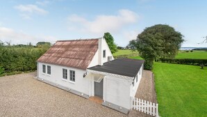 A white two-story house with a sloped roof, a gravel driveway, and a white picket fence. - 1 bedroom beautiful home in Roslev (Roslev)