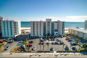 Een meerlaags hotel met een parkeerplaats en uitzicht op het strand.