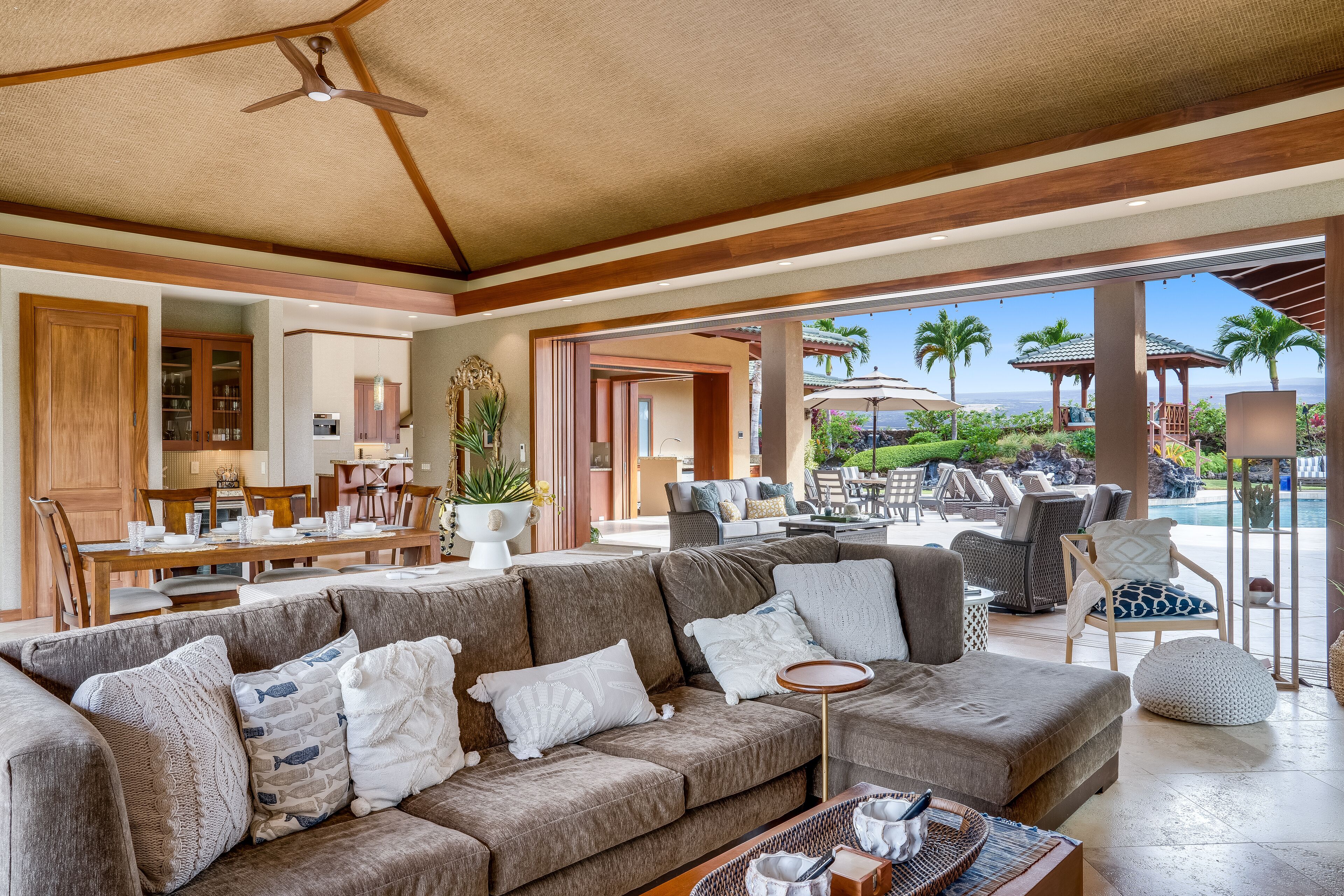 A spacious living area with a large sectional sofa, a dining table, and a view of the outdoor pool area.