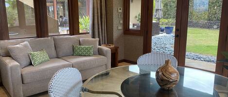 Una sala moderna con un sofá gris, cojines estampados, una mesa de centro de cristal y sillas de mimbre.