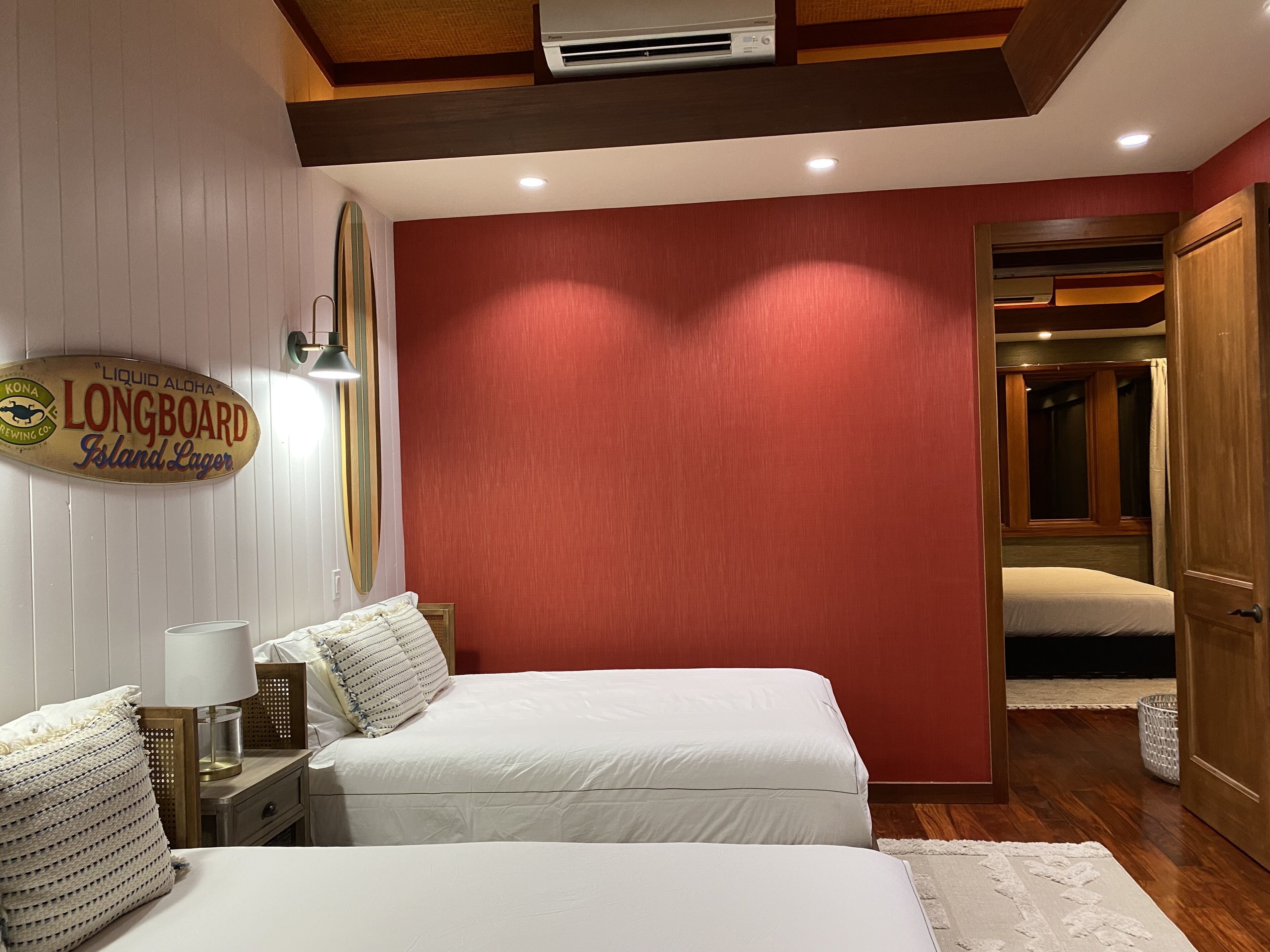A hotel room with two beds, a surfboard sign, and a wooden ceiling.