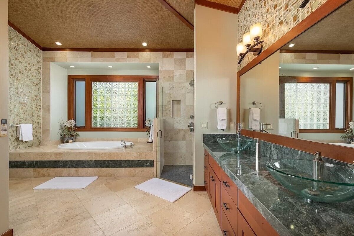A bathroom with a large bathtub, a glass-enclosed shower, and a vanity with a glass bowl sink.