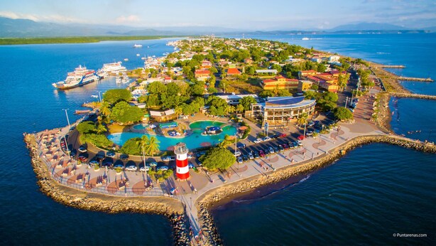 Vue aérienne d’une ville côtière avec une piscine centrale, un phare et un port de plaisance rempli de bateaux.