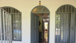 Un couloir avec une porte donnant sur une pièce, un sol carrelé et une fenêtre avec des barreaux.