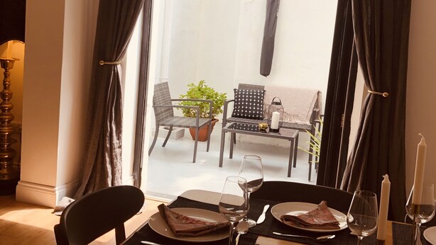 Un comedor con una mesa preparada para dos personas, una planta en maceta y vista a un patio exterior.
