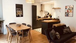 Una cocina moderna con comedor, que presenta una mesa y sillas de madera, un sofá negro y una lámpara colgante.