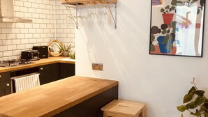 Una cocina moderna con encimera de madera, dos taburetes, una botellera colgante y una planta en maceta.