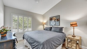 Une chambre à coucher avec un lit, des lampes de chevet, une commode et une fenêtre avec des stores.