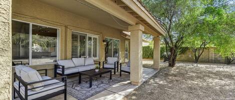 A covered patio area with outdoor furniture, including a sofa and chairs, and a coffee table.