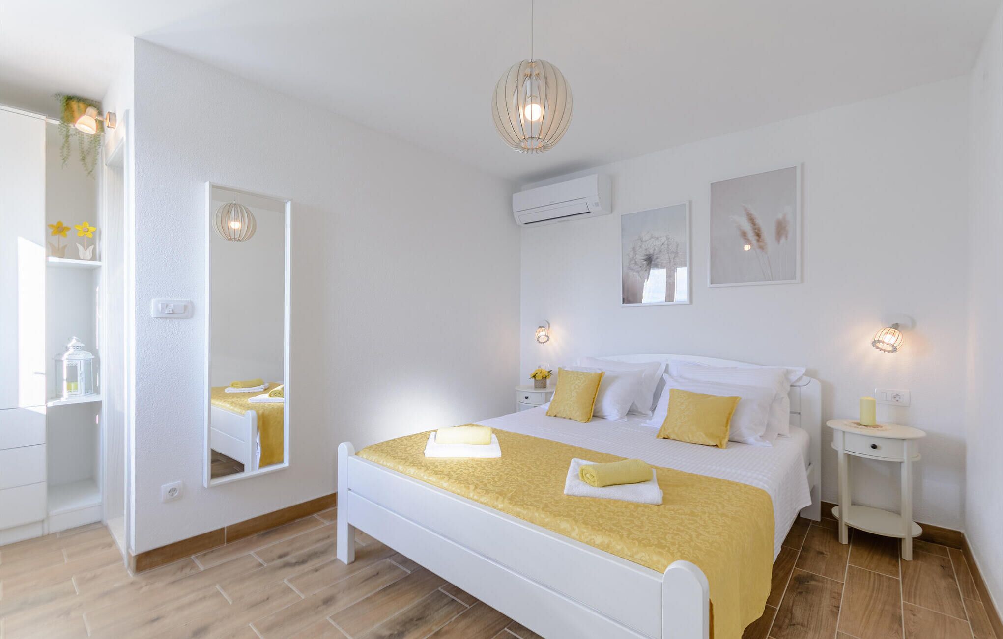 A bedroom with a bed, bedside tables, a mirror, and wall-mounted air conditioning unit.
