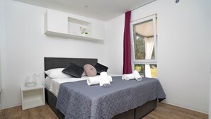 Un dormitorio moderno con cama, almohadas, una mesita de noche, una ventana con cortinas y un estante montado en la pared.