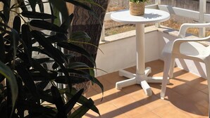 Un patio con una mesa y sillas blancas, una planta colgante y vistas al mar y a las montañas.