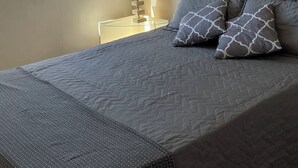Un dormitorio con cama, ventana, lámpara y un cuadro en la pared.