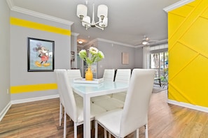 A dining area with a white table and chairs, a yellow accent wall, and a framed picture of a cartoon character.