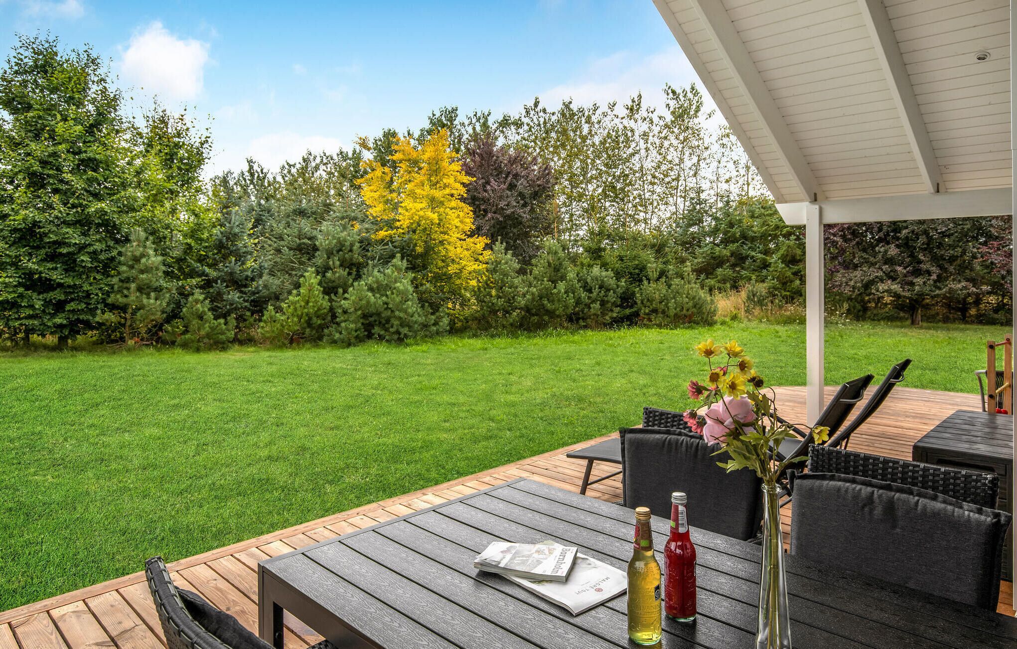 Une terrasse extérieure avec une table en bois, des chaises noires et un vase rempli de fleurs.