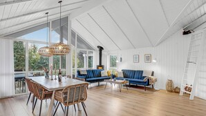 A spacious living area with a large window, a blue sofa, wicker chairs, and a wooden table. - Cozy home in Nexø with kitchen (Nexø)