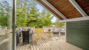 Une terrasse extérieure avec un plancher en bois, des meubles en osier et une vue sur les arbres.