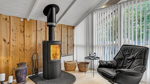 Un salon moderne avec un poêle à bois noir, un canapé en cuir et de grandes fenêtres équipées de stores verticaux.