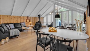 Un salon moderne avec un canapé en cuir noir, une table de salle à manger ronde entourée de chaises et un plafond en bois.