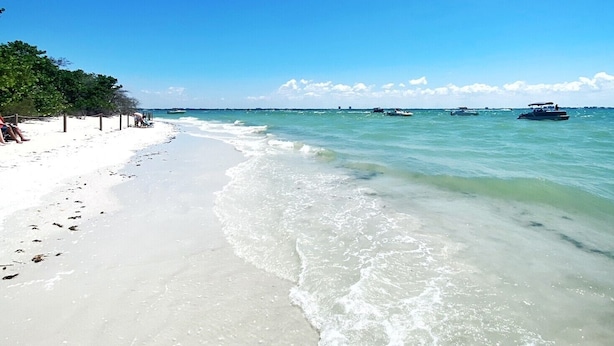 Una spiaggia con acque cristalline turchesi, una riva sabbiosa e alcune barche in lontananza.
