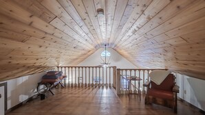 Een zolderkamer met hoge plafonds, houten balken, een houten vloer, een bank, een stoel en een klein tafeltje.