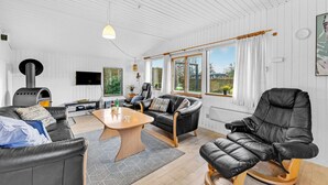 A spacious living room with a fireplace, leather sofas, a coffee table, and large windows offering a view of the outdoors.