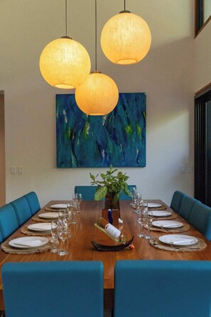 A dining area with a wooden table set for eight, blue upholstered chairs, and three hanging pendant lights.
