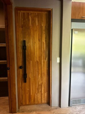 A wooden door with a black handle, a metal door frame, and a refrigerator to the right.