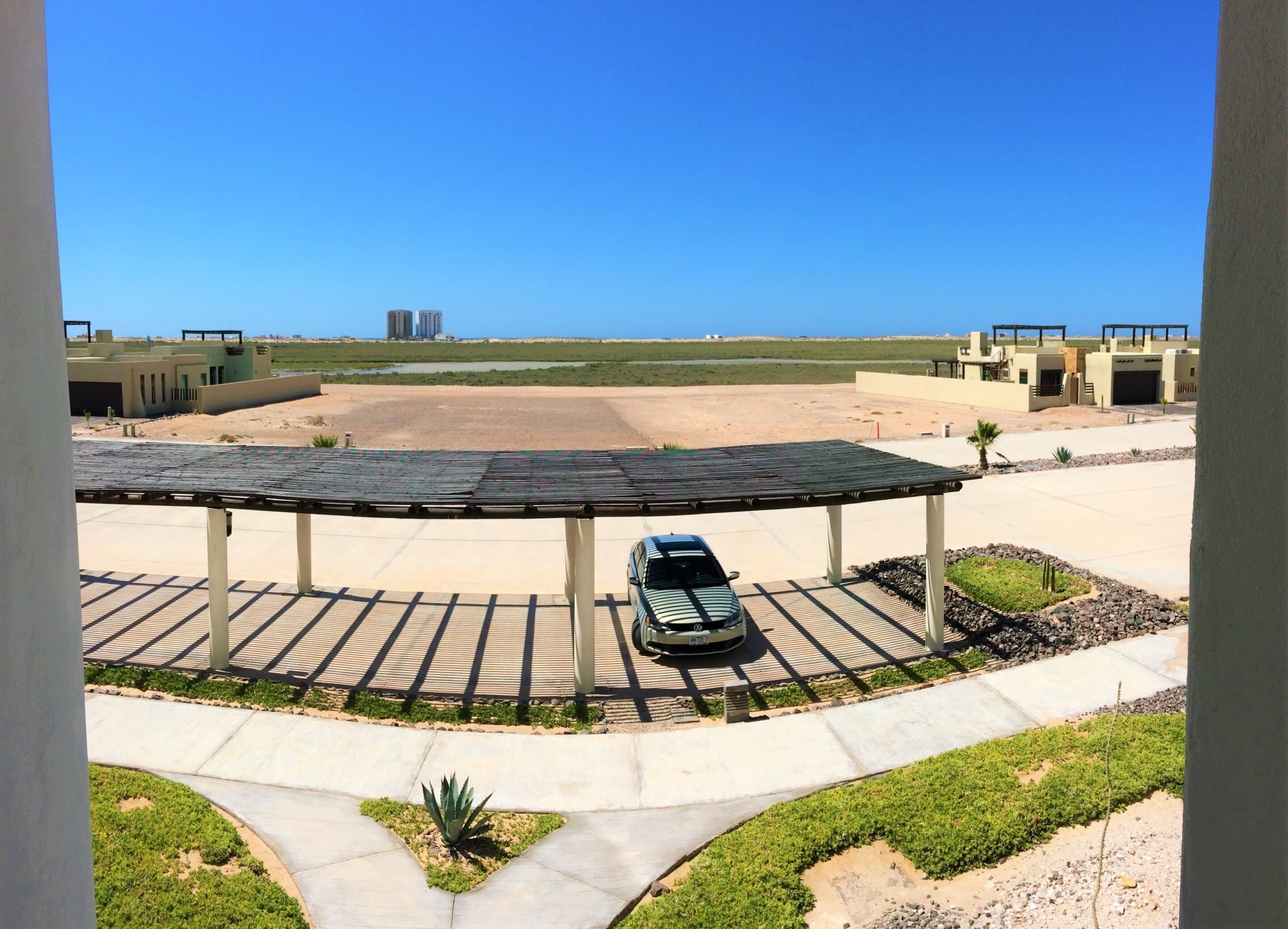 Un estacionamiento techado con un coche, vista a la playa y edificios al fondo.