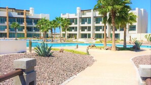 Un hotel moderno con zona de piscina, palmeras y un cielo azul despejado.