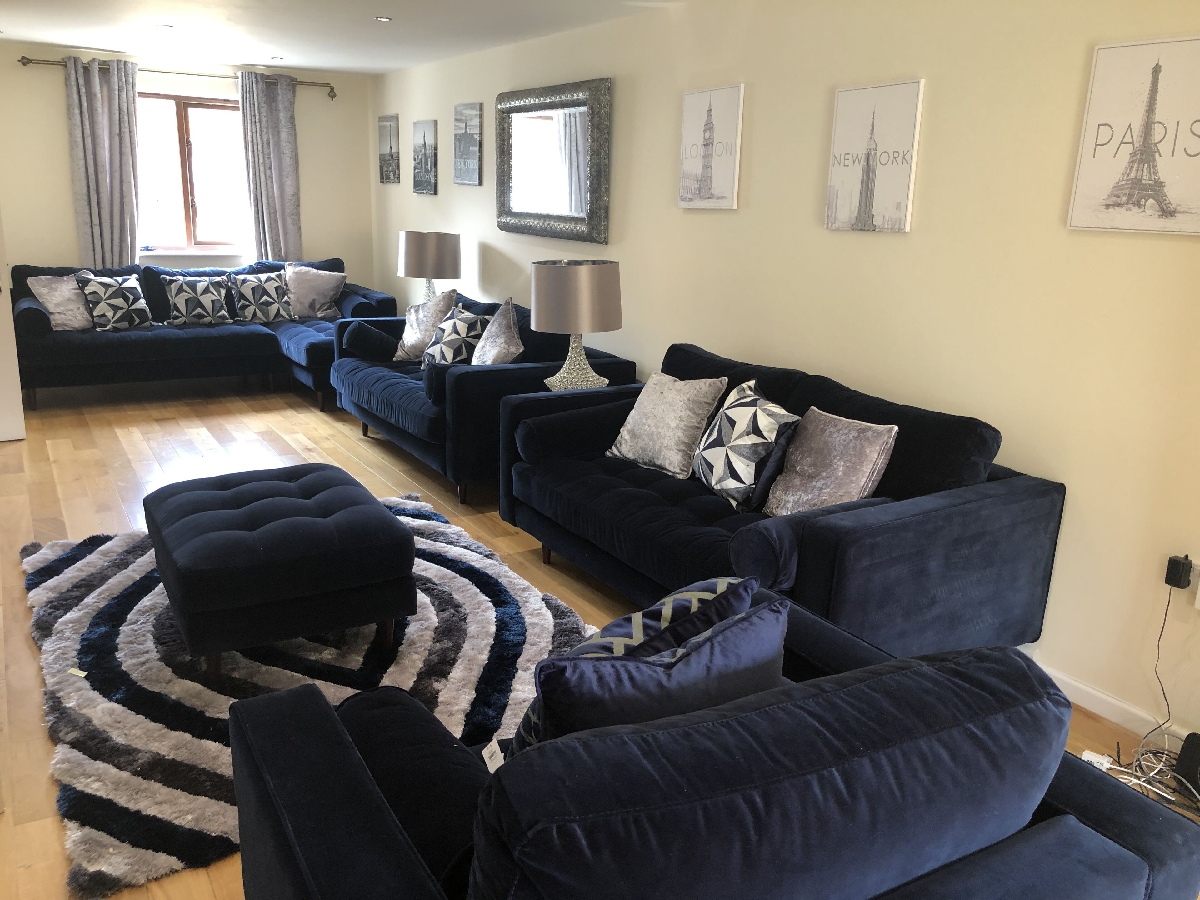 A living room with two dark blue sofas, a patterned rug, and cityscape wall art.