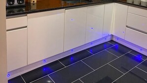 A modern kitchen with white cabinets, a black countertop, and blue under-cabinet lighting.