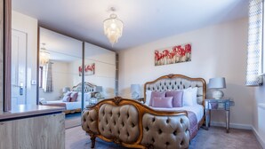 A spacious bedroom with a large bed, a chandelier, a mirror, and a painting on the wall.