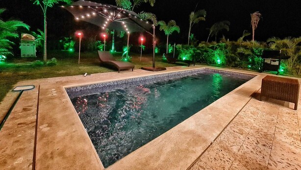 Ein Schwimmbecken mit Liegestühlen und einer Pergola mit Lichterkette.
